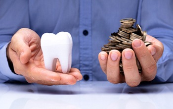 An individual holding a model tooth in one hand and a handful of change in the other