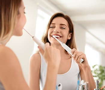 A young woman standing at the mirror and brushing her teeth with an electric toothbrush