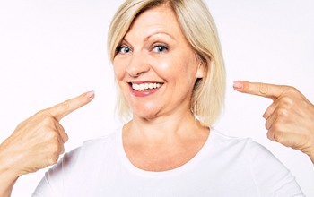 An older woman pointing to her smile and pleased with her new dental implants in Carrollton