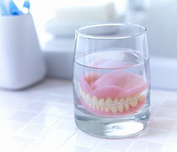 A full set of dentures soaking in a glass of water and denture cleaner