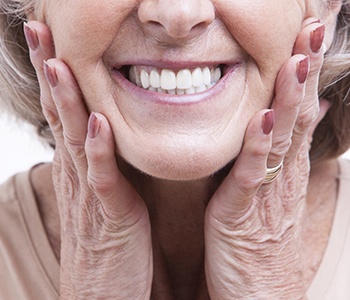 An up-close look of an older woman’s dentures while holding her face between her hands