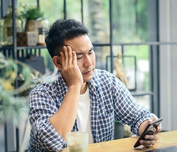 Man with toothache in Carrollton looking at his phone