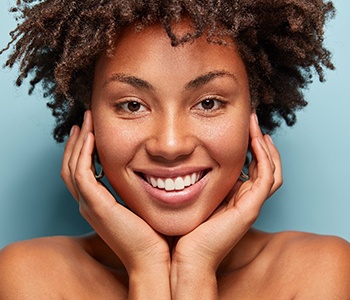 A young female holding her face between her hands after receiving teeth whitening treatment